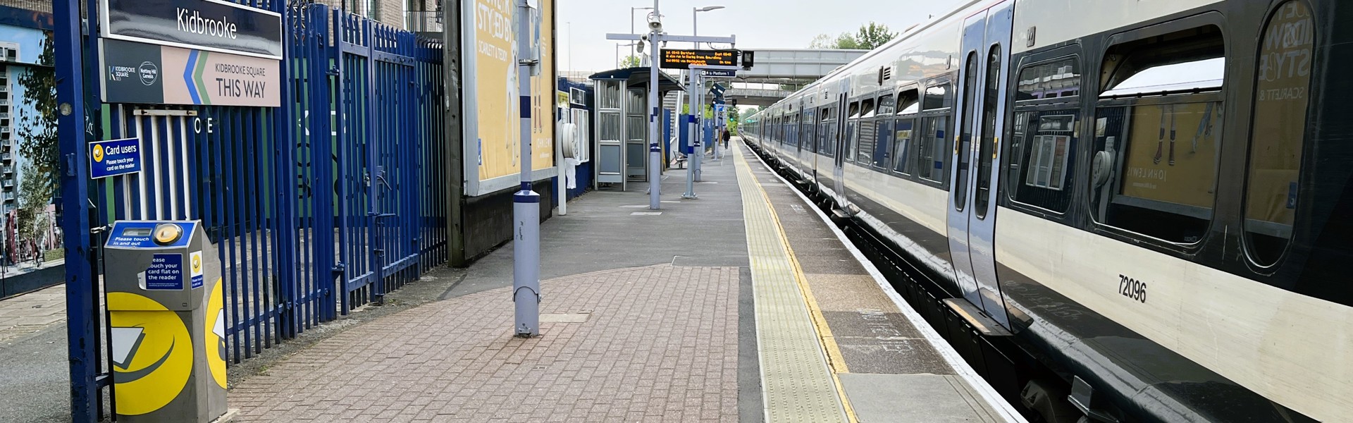 Looking along Kidbrooke Train Station with a Southeastern train arrived at the platform. Kidbrooke Square signage on show points to the exit. 